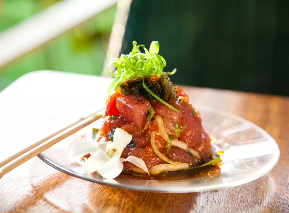 Plate of Hawaiian poke garnished with green onions, seaweed, and edible flowers, served as a pupu or appetizer.